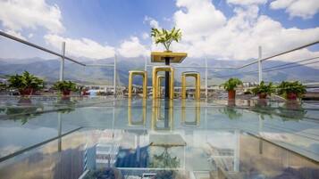 Terraza en la azotea con piso de vidrio, plantas en macetas y vistas despejadas a las montañas.