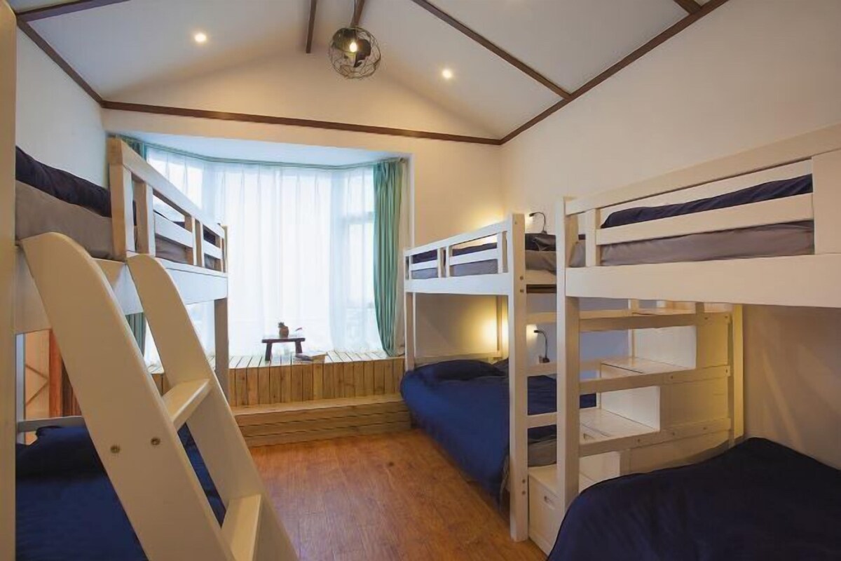 A bunk bed room with a desk and chair, a window with curtains, and a ceiling light.