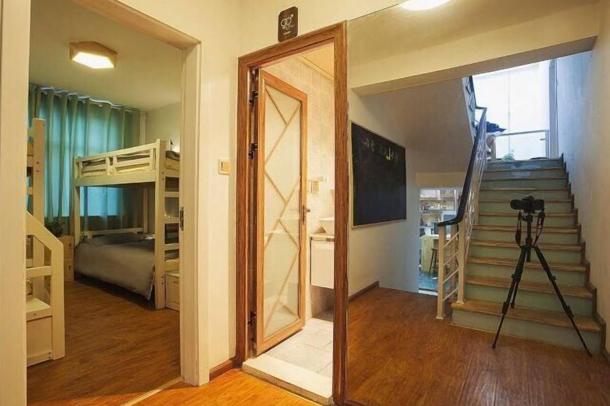 A room with a bunk bed, a wooden door, a staircase, and a tripod.