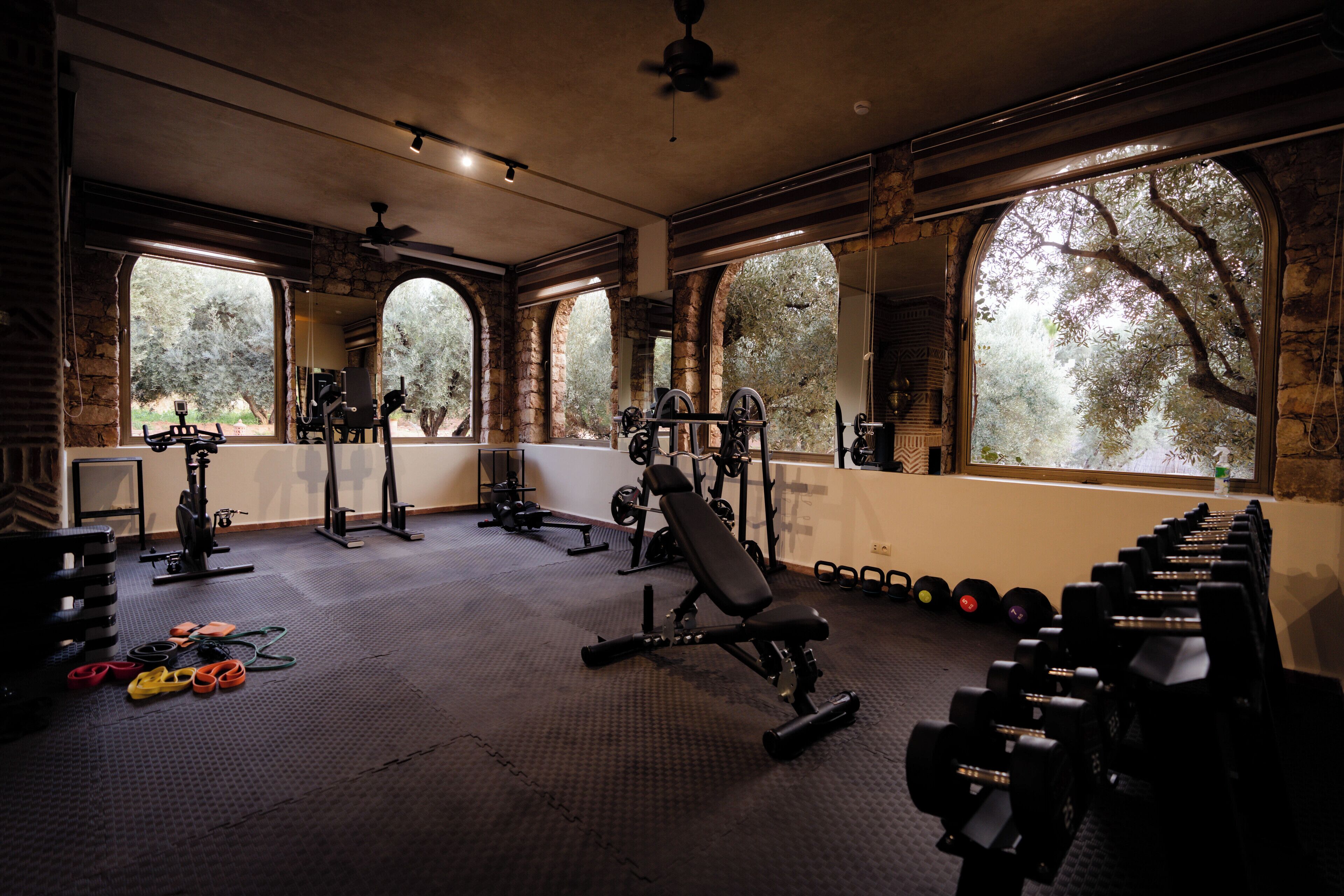 A gym with stone walls, large windows, and various exercise equipment.