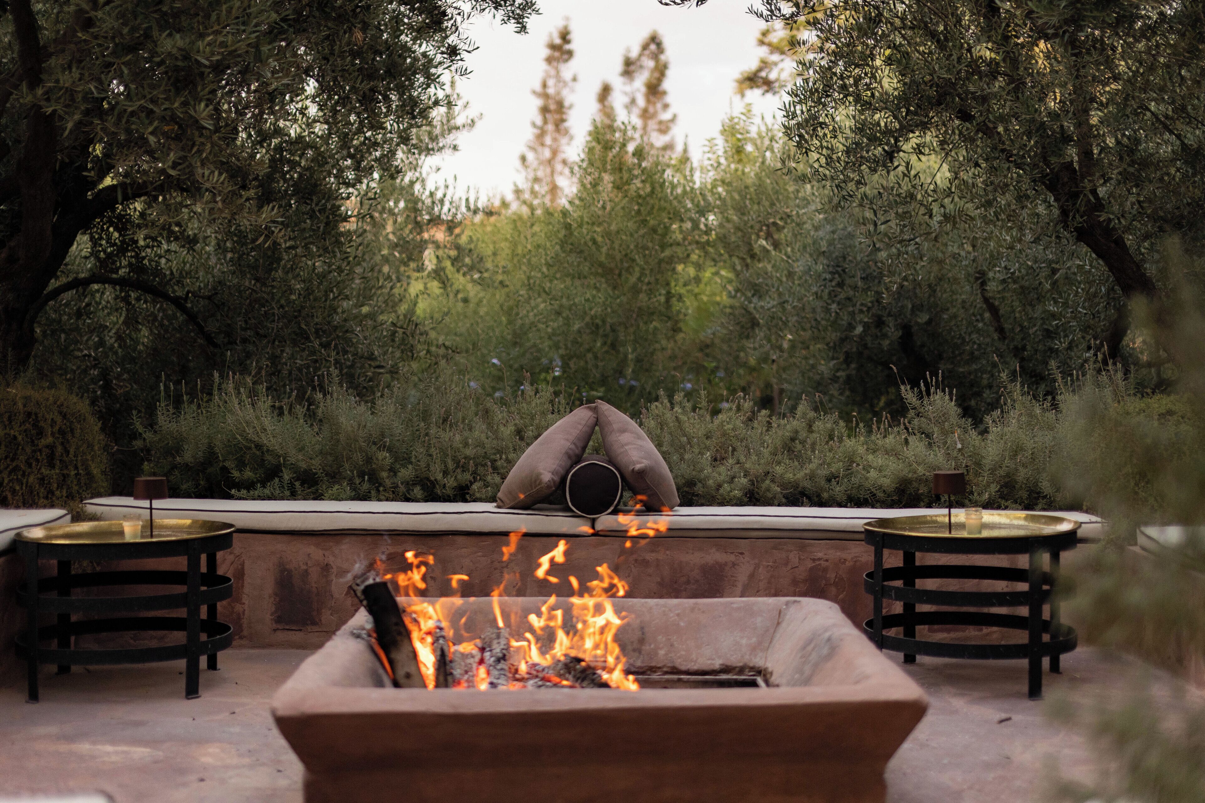 An outdoor seating area with a fire pit, two round tables, and a cushioned bench.