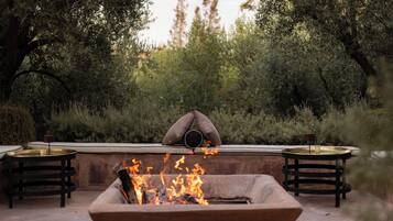 An outdoor seating area with a fire pit, two round tables, and a cushioned bench.