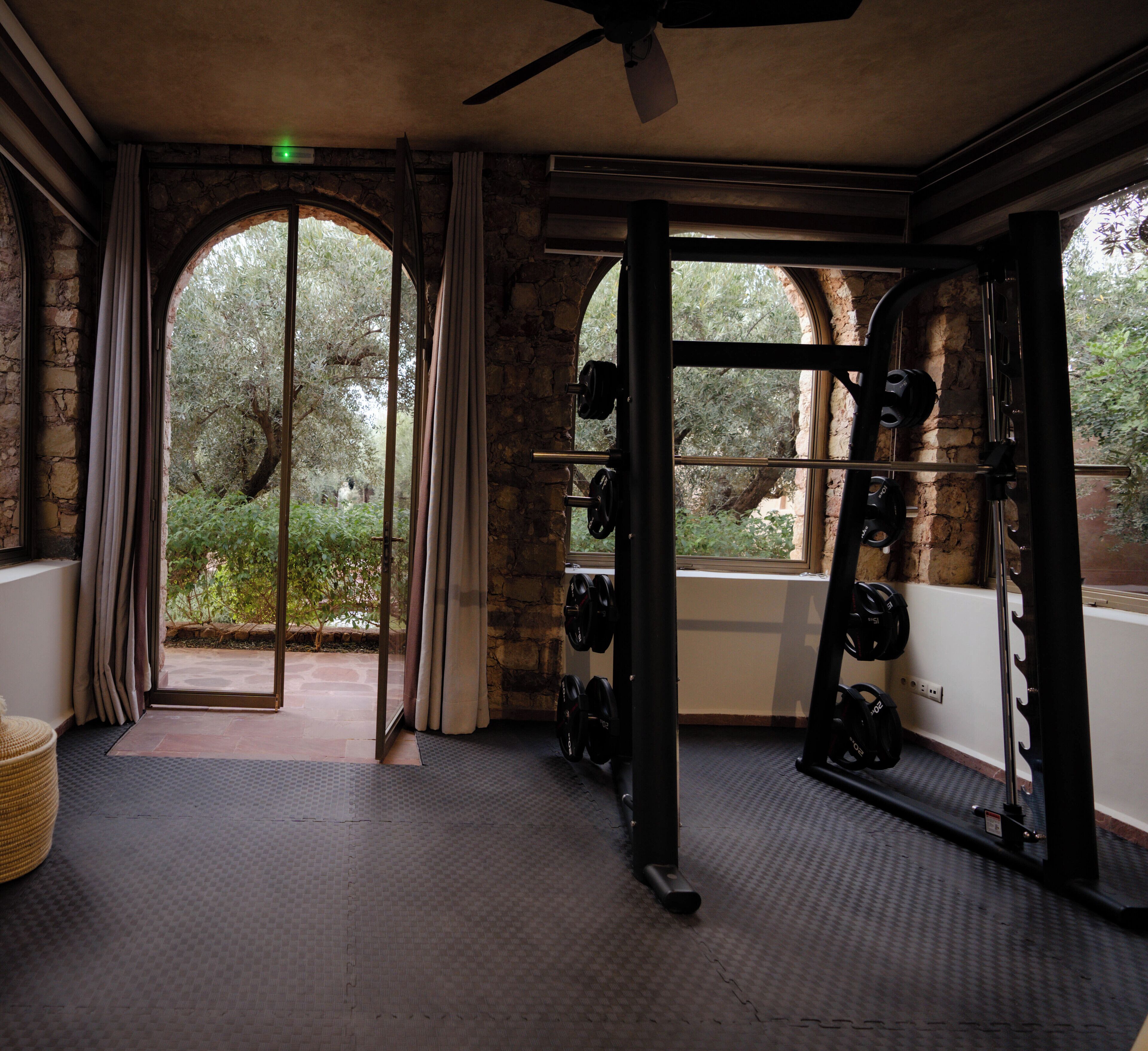 A gym with a stone wall, a ceiling fan, and a view of trees through a large window.