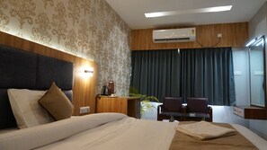 A hotel room with a large bed, a desk with a chair, an air conditioning unit, and a mirror. - HOTEL SATKAR (Katihar)