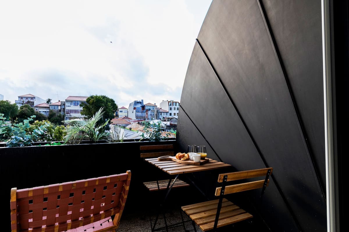 Un balcón con una mesa y sillas de madera, vistas a edificios y una planta en maceta.