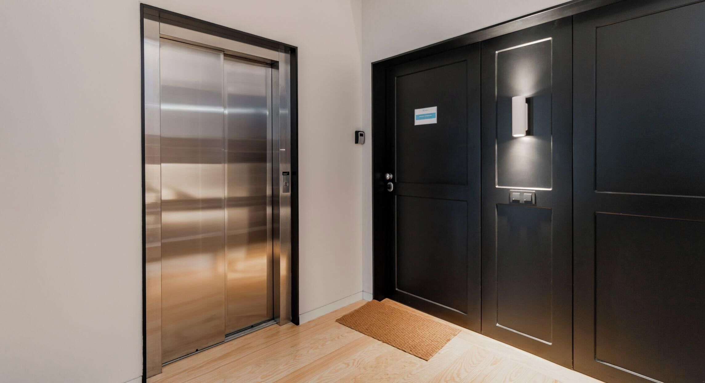 A modern elevator and a dark door with a light fixture.