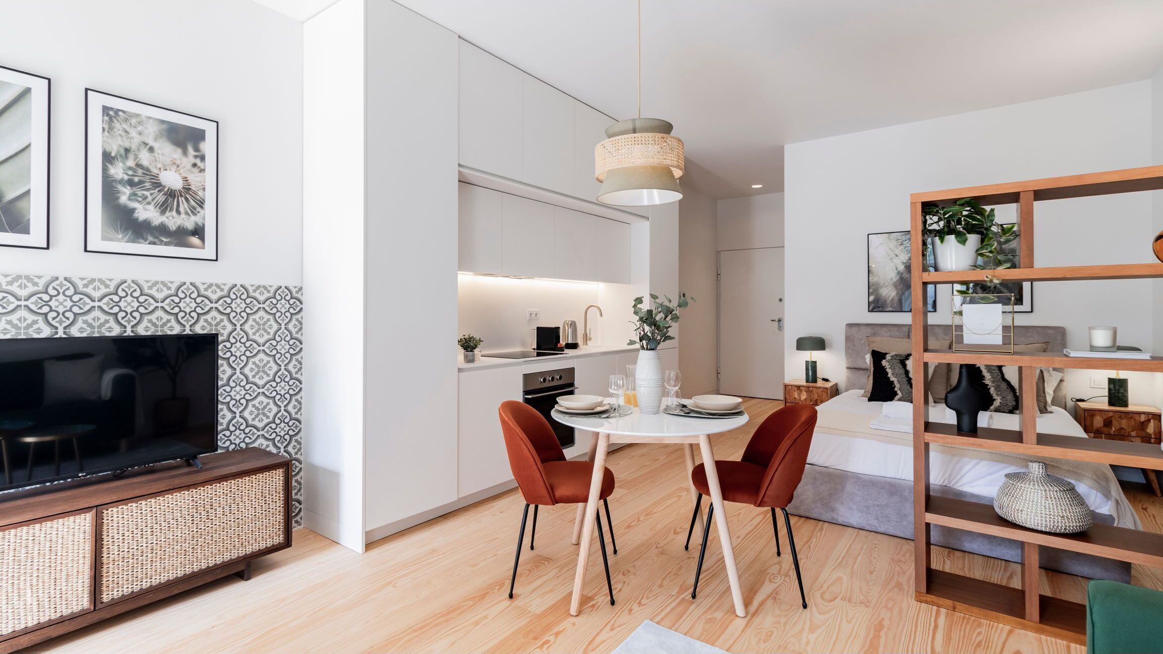 A modern living room with a TV, dining area with chairs, and a kitchen in the background.