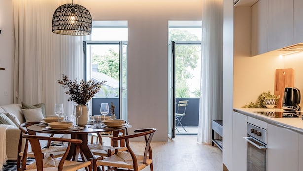 A modern kitchen with white cabinets, a built-in oven, and a dining area with a round table and wooden chairs. - Almada 551 by LovelyStay (Porto)