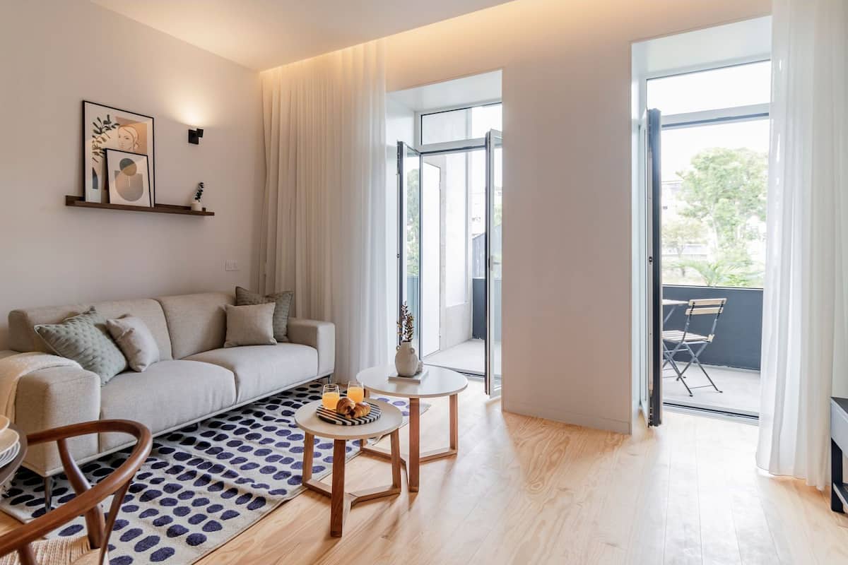Una sala de estar moderna con sofá, mesa de centro y comedor. Hay un ventanal que proporciona luz natural y vistas al exterior.