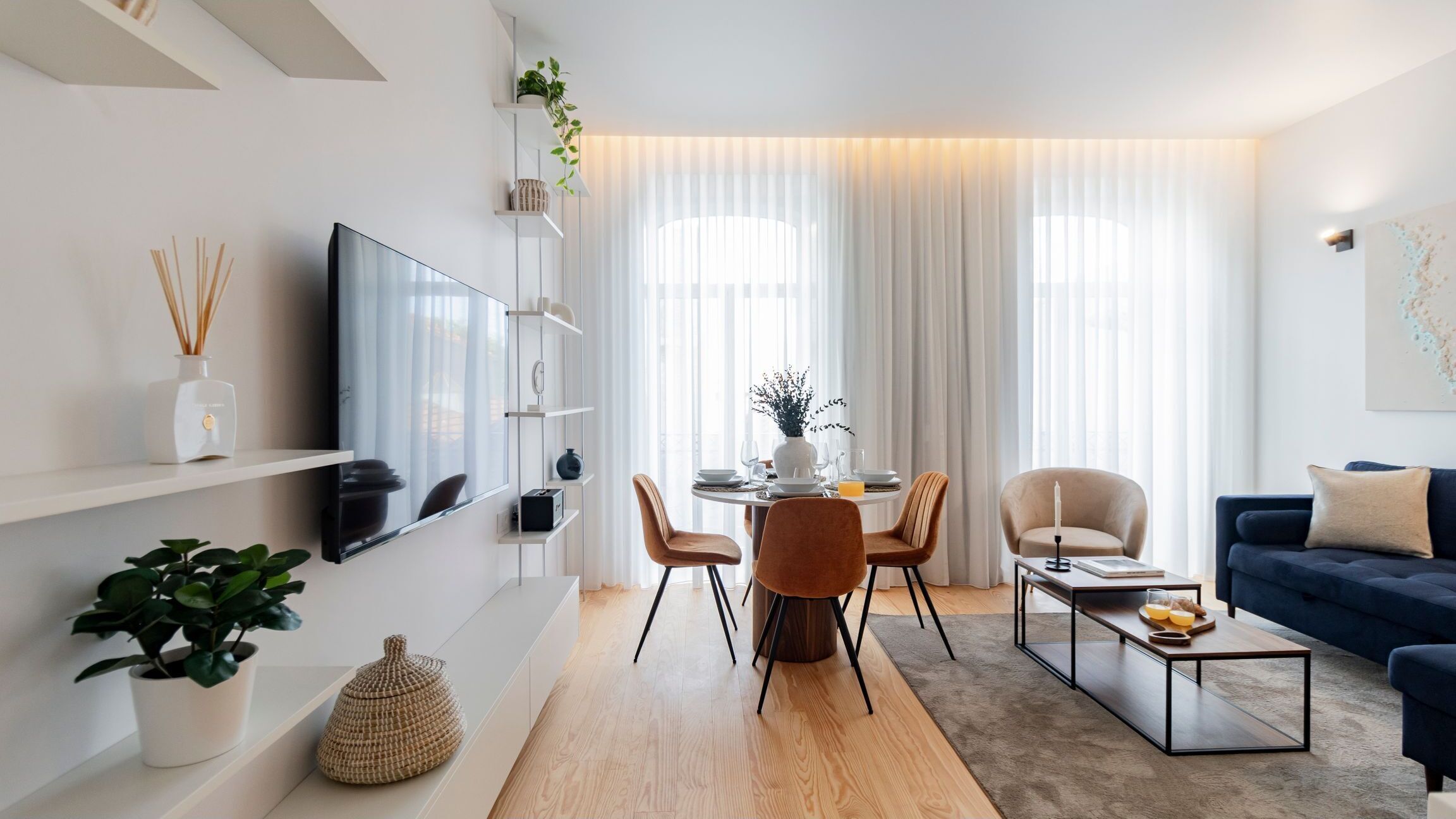 En moderne stue med et fladskærms-tv, et spiseområde med et rundt bord og stole, en sofa og et sofabord.