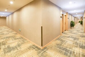 A hotel corridor with patterned carpet, doors, and potted plants. - Jiejiao 33 Qinglv Hotel (Chongqing)