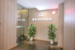 Un espace d’accueil d’hôtel avec un mur en bois, deux plantes en pot et une porte vitrée donnant sur l’intérieur.