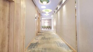 A hallway with a patterned carpet, wooden paneling on the left, and recessed lighting on the ceiling. - Jiejiao 33 Qinglv Hotel (Chongqing)
