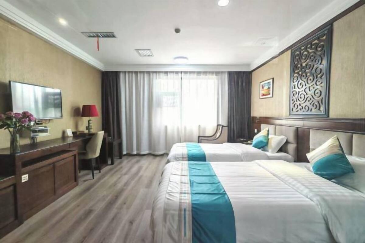 A hotel room with two beds, a desk with a chair, a TV, and a decorative wall panel.
