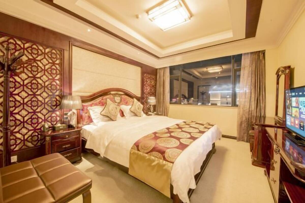 A hotel room with a large bed, a desk, a TV, and a window with a view.