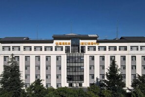 A large, multi-story building with a symmetrical facade, featuring a central entrance with a glass door and a series of windows on each floor. - General Fenghua (Lijiang) Travel Center (Lijiang)