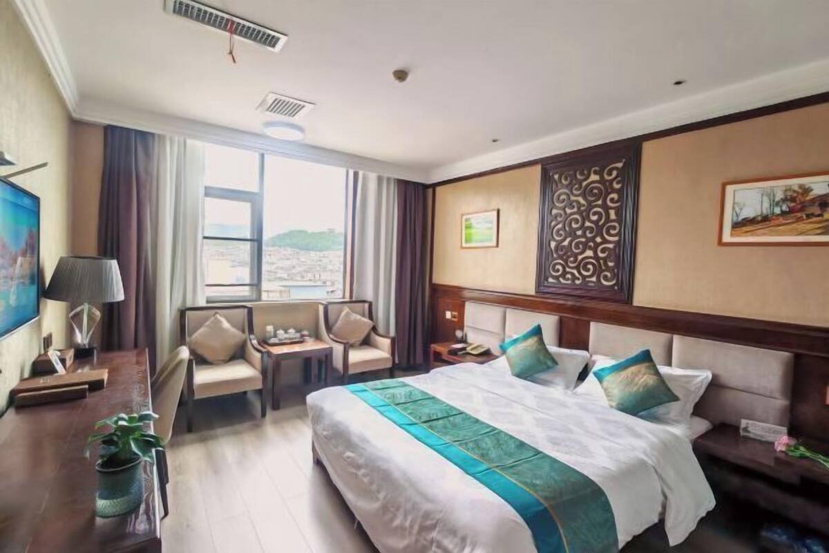 A hotel room with a large bed, a desk, a chair, a nightstand, and a window with a view.