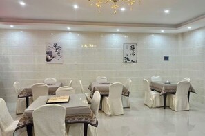 A dining area with multiple tables and chairs, each with a tablecloth and chair covers. - General Fenghua (Lijiang) Travel Center (Lijiang)