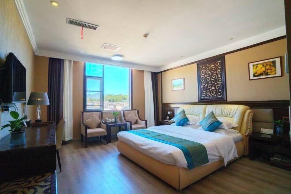 A hotel room with a large bed, a desk, a chair, a small table, and a window with a view.