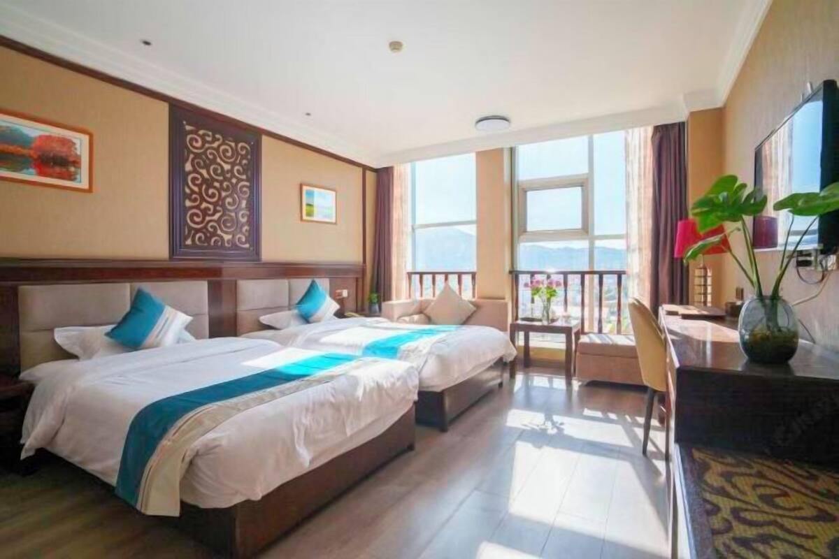 A hotel room with two beds, a balcony with a view, a desk, and a TV.