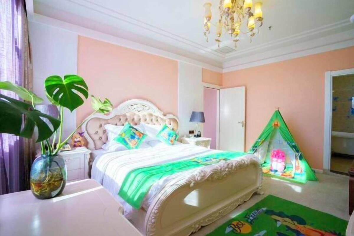 A bedroom with a bed, a bedside table, a lamp, a green tent, and a plant.