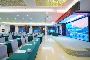 A conference room with rows of tables and chairs, a stage with a large screen, and a red sign above the stage. - General Fenghua (Lijiang) Travel Center (Lijiang)