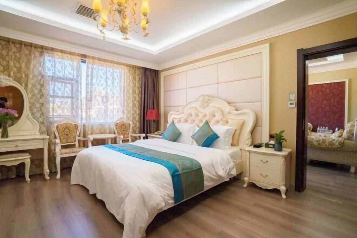 A bedroom with a large bed, a bedside table, a chair, a desk, and a mirror.