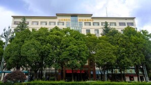 A multi-story building with a central entrance, surrounded by lush green trees. - General Fenghua (Lijiang) Travel Center (Lijiang)