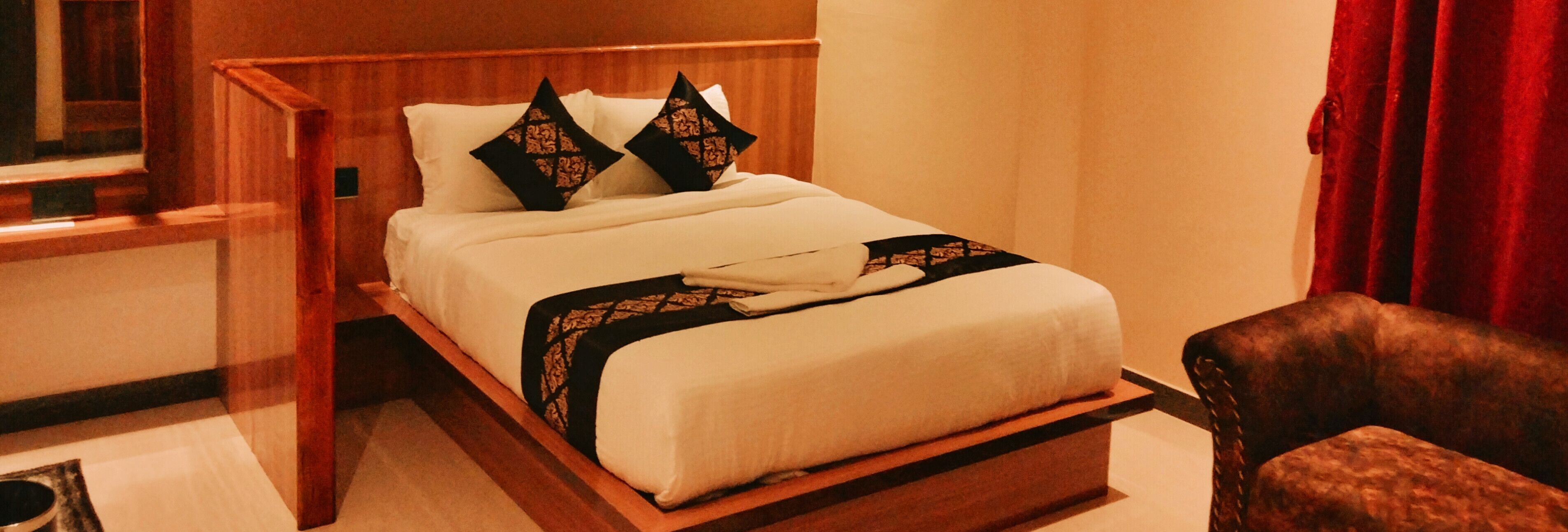 Una cama bien hecha con estructura de madera, dos almohadas decorativas y una toalla doblada sobre la cama.