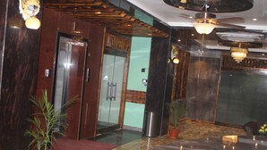 A lobby with a reception desk, a glass elevator, a trash bin, and a potted plant. - Hotel Red Crown Pvt Ltd-Bardibas (Bardibas)