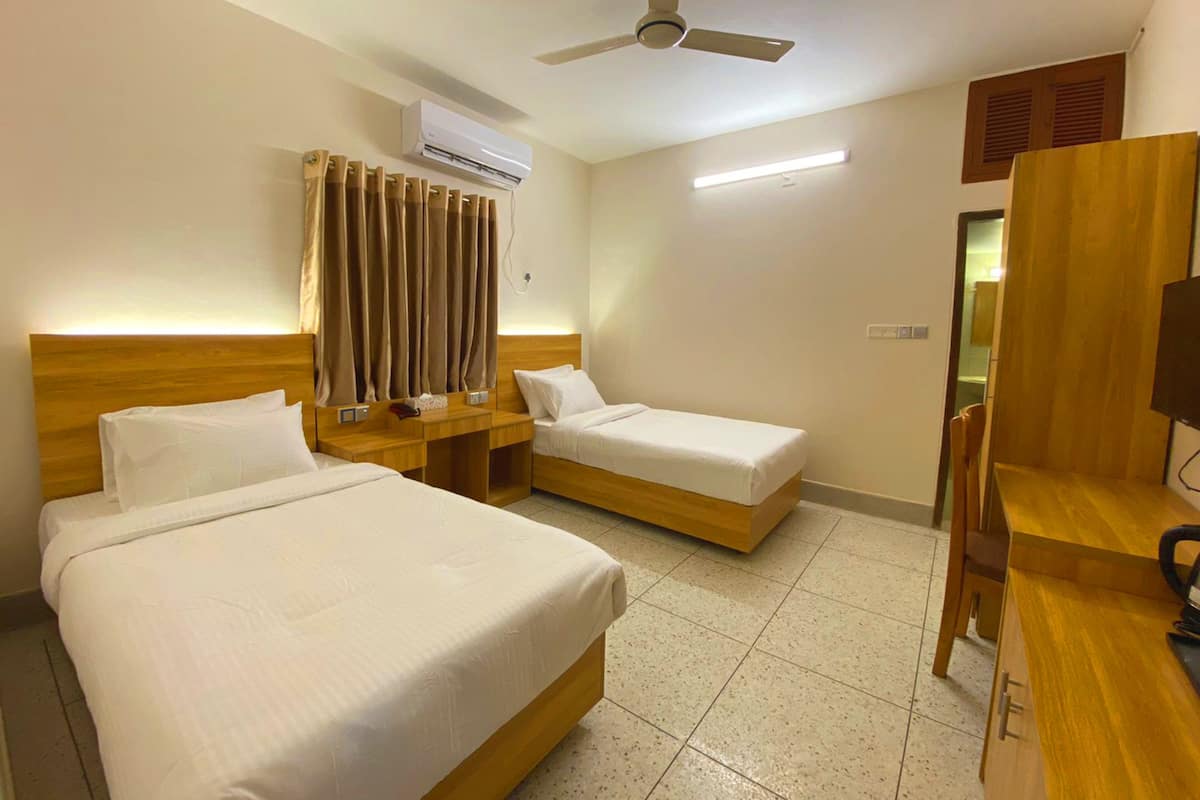 A hotel room with two beds, a ceiling fan, an air conditioning unit, a desk with a chair, and a television.