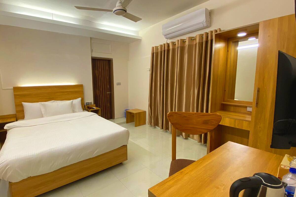 A hotel room with a wooden bed, a desk with a chair, a television, and an air conditioning unit.
