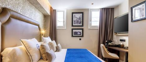 Una habitación de hotel con una cama grande, un escritorio, una silla y dos cuadros en la pared.