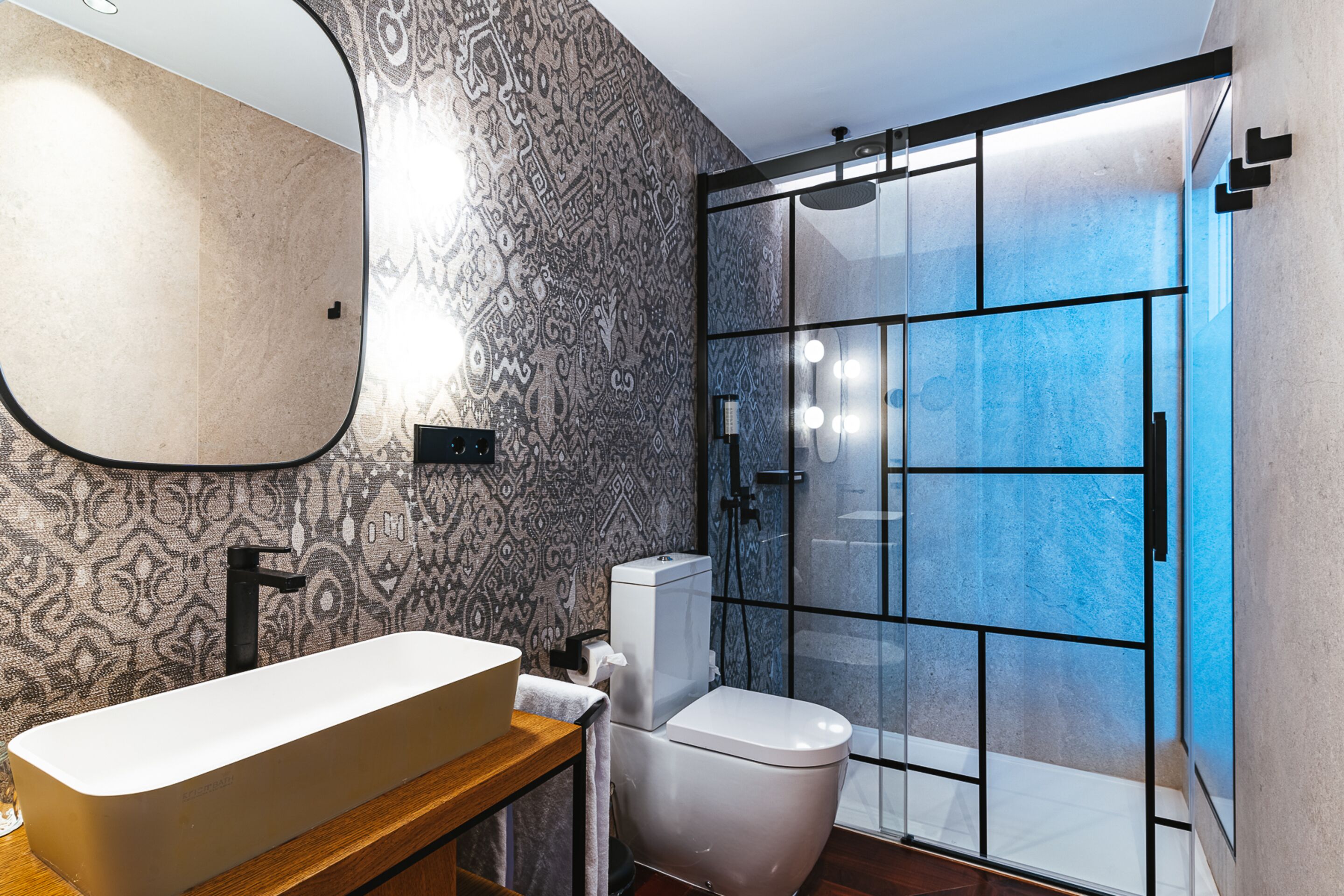 A modern bathroom with a large mirror, a freestanding sink, a toilet, and a glass-enclosed shower area.