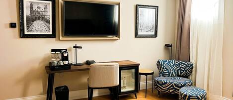 Una habitación de hotel con escritorio, silla, reposapiés y dos cuadros en la pared.