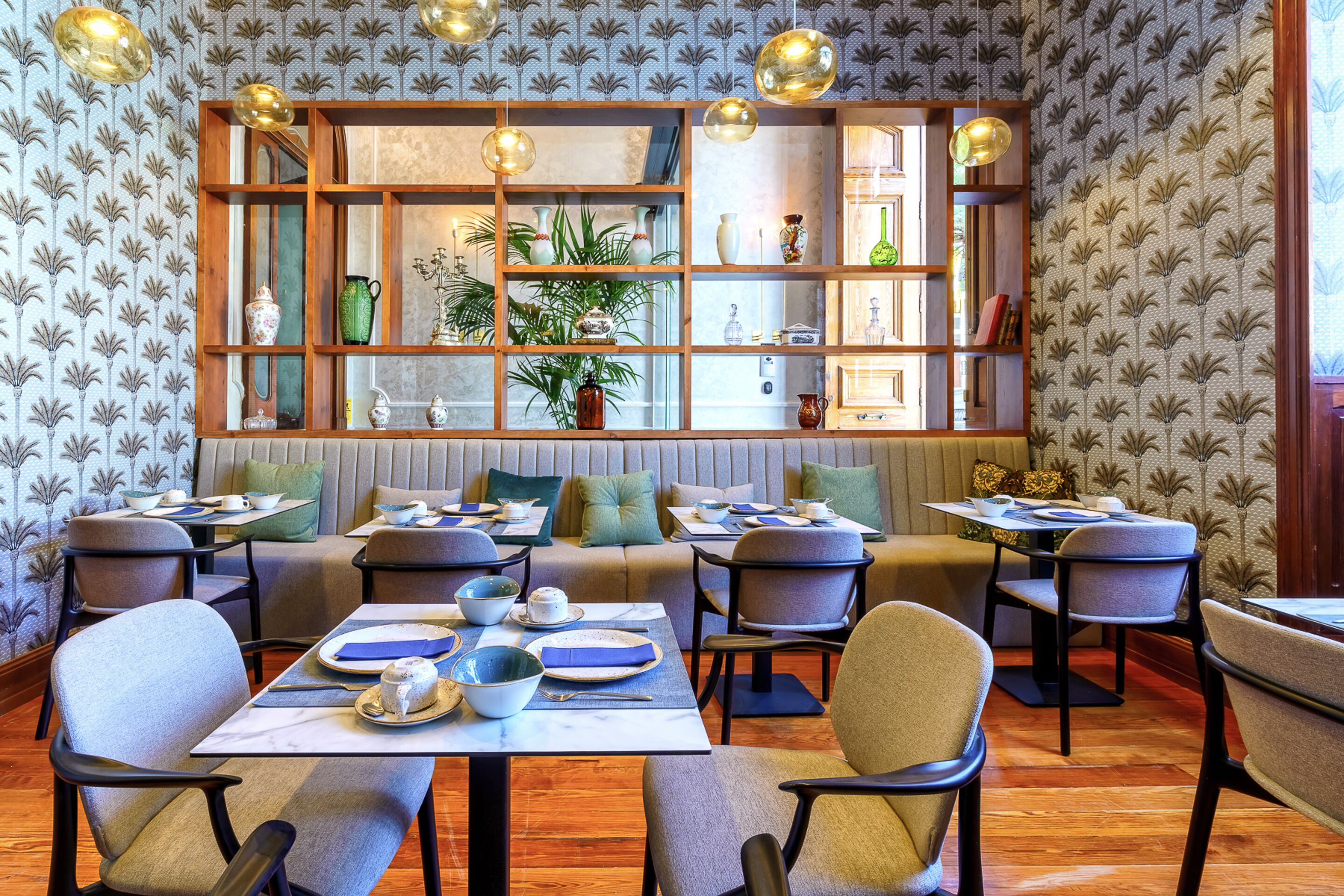 A restaurant with a wooden bookshelf, tables, chairs, and a patterned wallpaper.