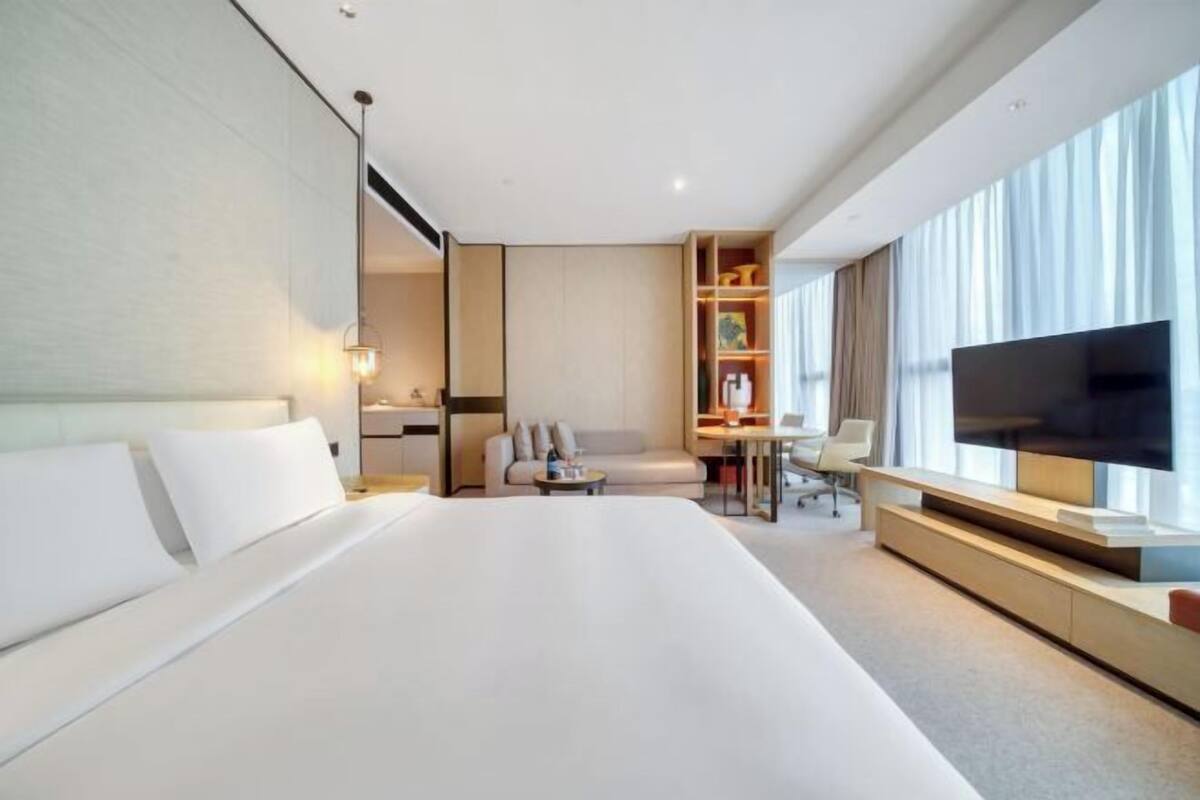 Una habitación de hotel moderna con una cama grande, televisión, escritorio y zona de estar.
