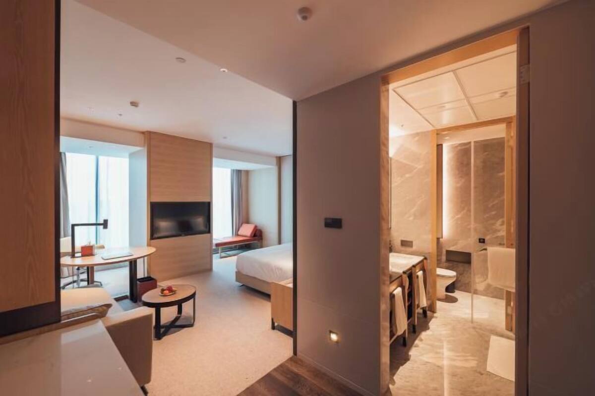 Una habitación de hotel moderna con cama, un pequeño rincón de descanso, televisión y baño con piso de mármol.