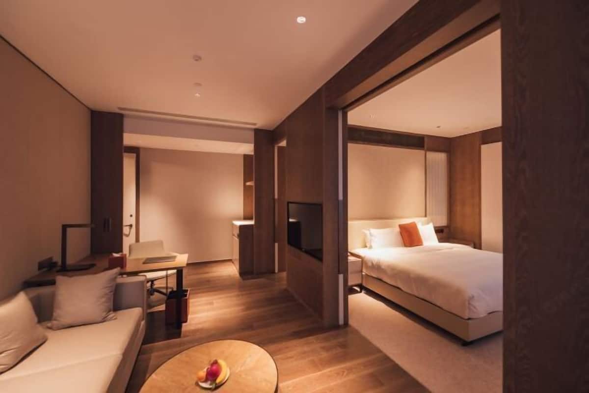 Una habitación de hotel moderna con sofá, cama, televisión y una mesita con fruta.