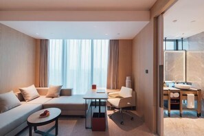 A modern hotel room with a sofa, a small table, a chair, a desk, and a bathroom area with a mirror and sink. - Zhenhe Yiting Hotel (Ningbo)