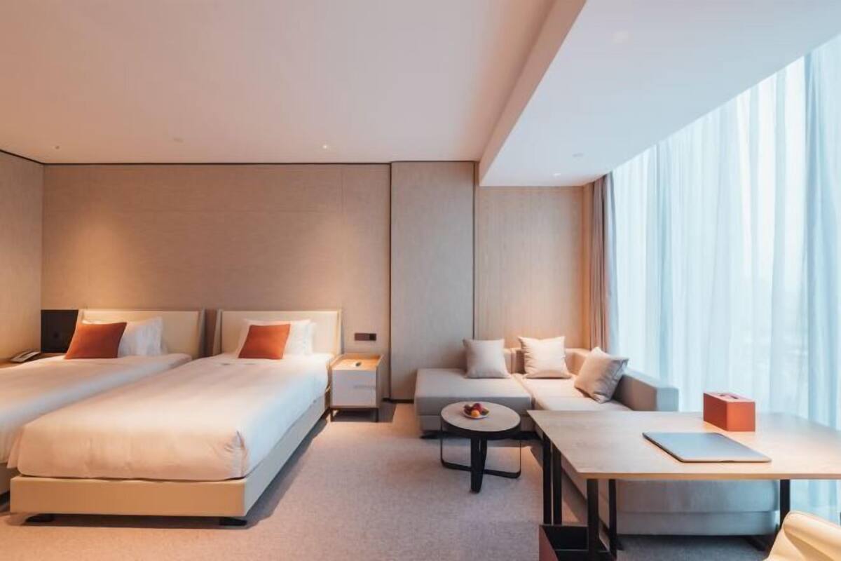 Una habitación de hotel moderna con dos camas, un sofá, una mesita y un ventanal con cortinas.