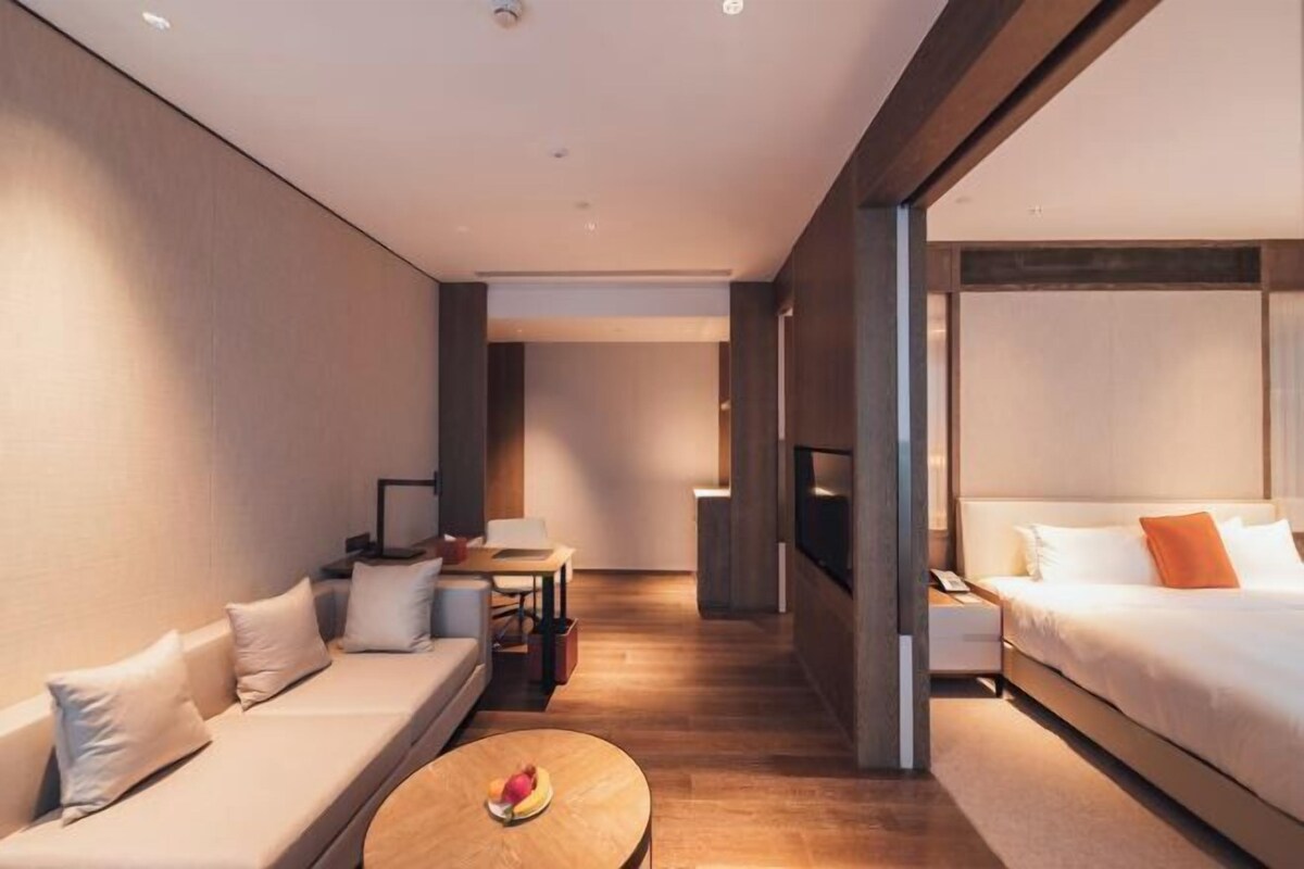 A modern hotel room with a sofa, a small table with fruit, a bed, and a TV.