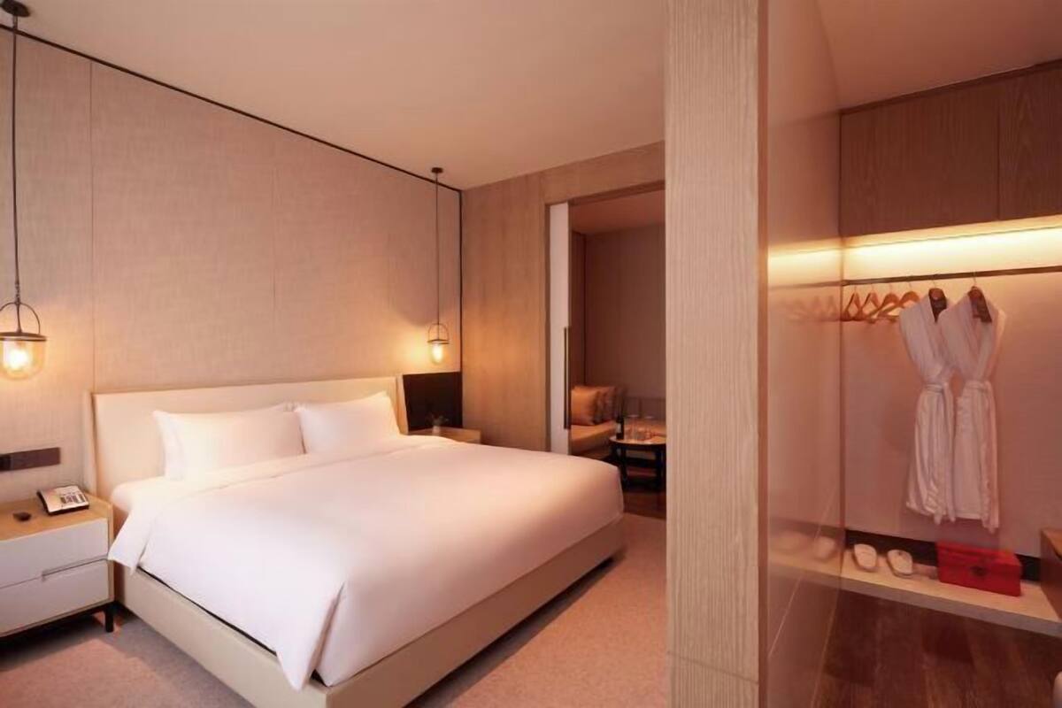 Una habitación de hotel con una cama grande, mesitas de noche, un armario y una presentación de bata y pantuflas.