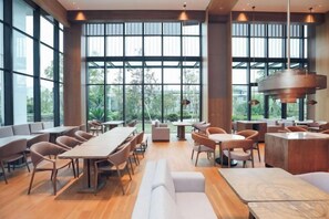 A spacious indoor area with tables and chairs, large windows, and a modern ceiling light fixture. - Zhenhe Yiting Hotel (Ningbo)