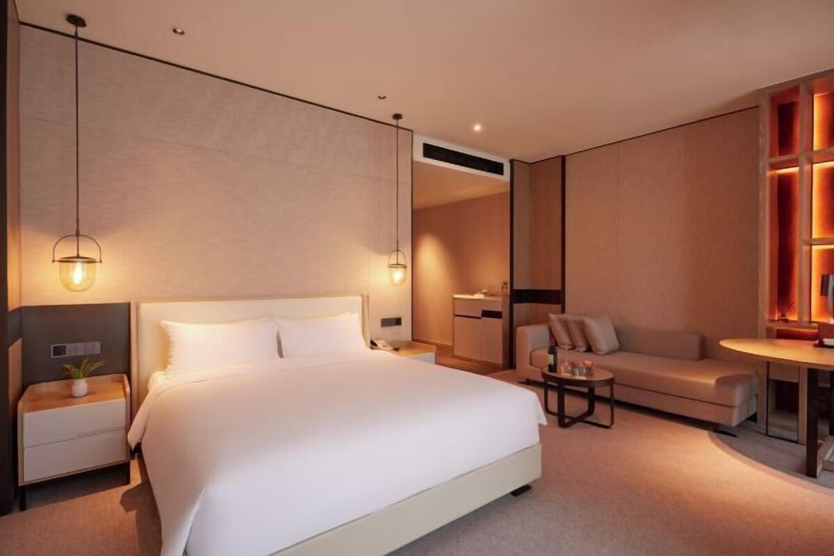 A modern hotel room with a large bed, bedside tables, a sofa, and a small table.