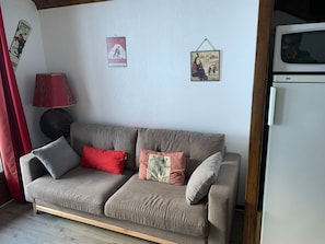 A living room with a grey sofa, red and checkered pillows, a red lamp, and wall art depicting skiing and a sports shower. - Duplex for 8 with WiFi, balcony and parking in Valloire (Valloire)