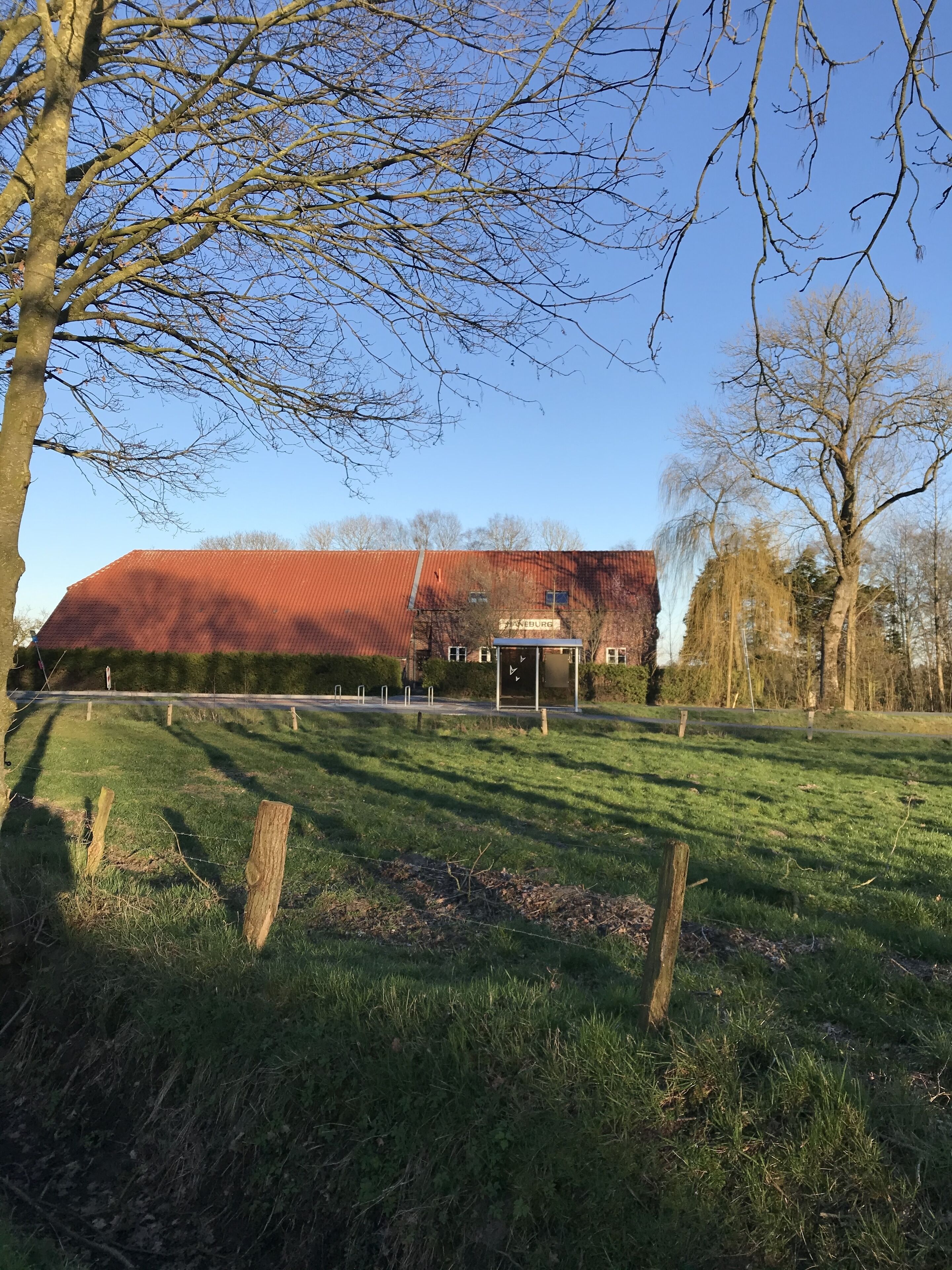 A rural setting with a barn, a bus stop, and a fenced area.