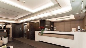 A modern reception area with a reception desk, a plant, and a wall-mounted information board.