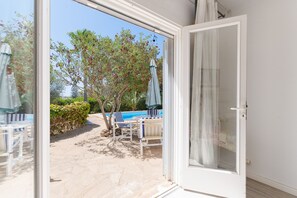 Porta de correr de vidro aberta, dando para um pátio com piscina, cadeiras de descanso e uma árvore com frutos vermelhos.