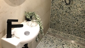 A bathroom with a white sink, a mirror, and a shower with a mosaic tile wall.